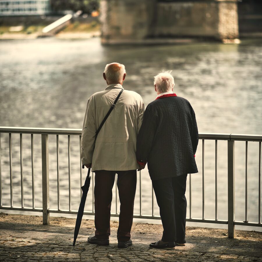 An older couple holding hands as they look out over a river