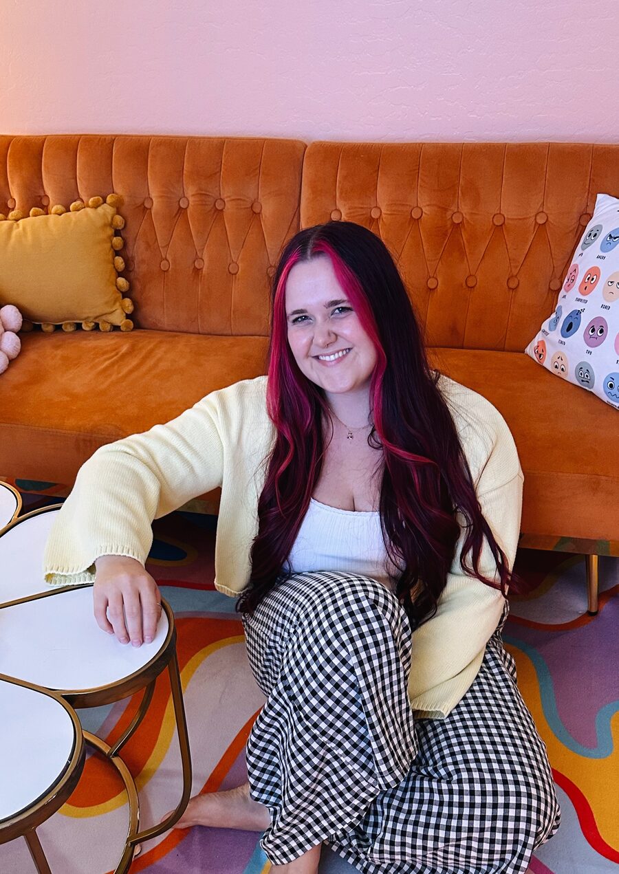 Kerstyn smiling, seated on an orange velvet couch in her warm, colorful office