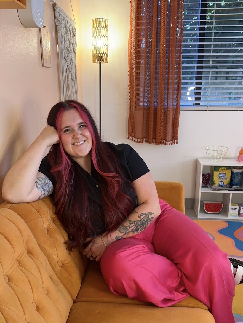 Kerstyn Ludlow, LAMFT, smiling on a mustard velvet couch in her warm, colorful office