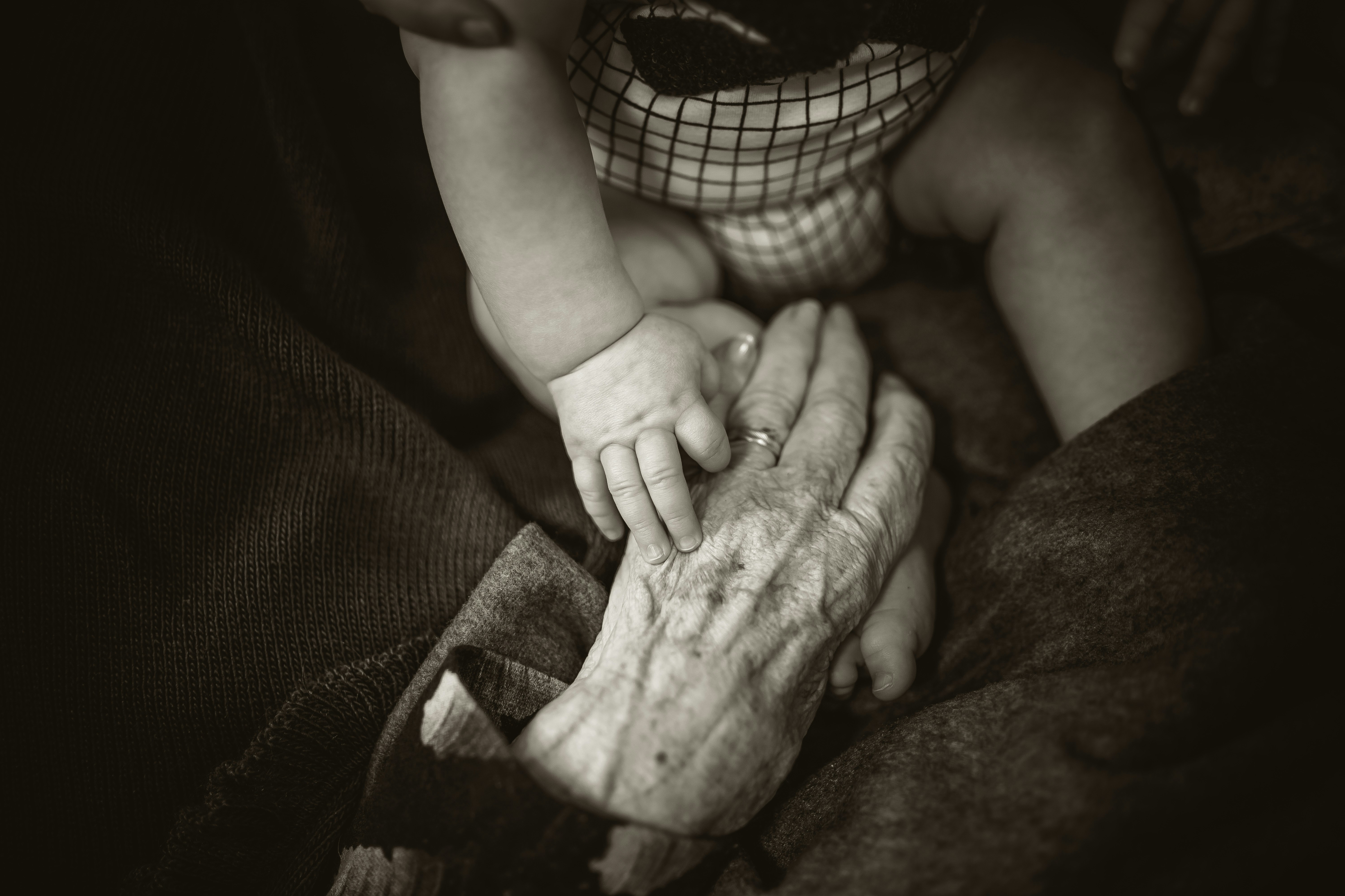 A baby's hand resting on an elder's hand — three generations